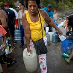 A woman carries a container with water collected from an open pipe above the Guaire River, during rolling blackouts which affects the water pumps in people's homes, offices and stores, in Caracas, Venezuela. </br>(Ariana Cubillos/AP/Shutterstock)